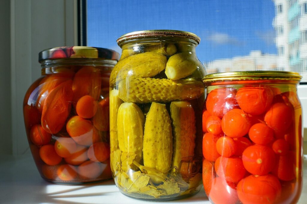 3 bocaux de conserve de légumes contenant des cornichons des tomates et des carottes